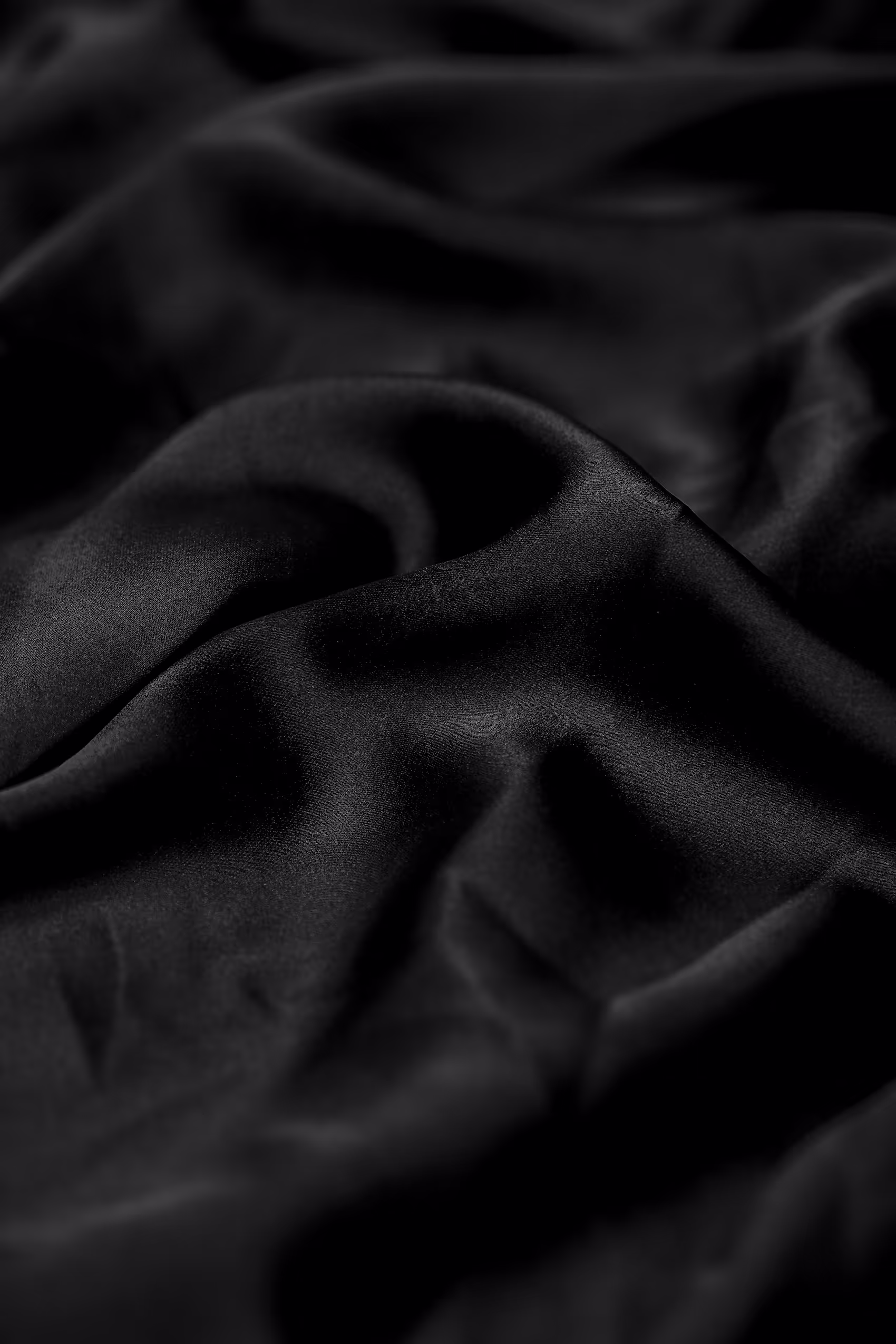 Close-up of smooth, black satin fabric with gentle folds and a soft sheen.