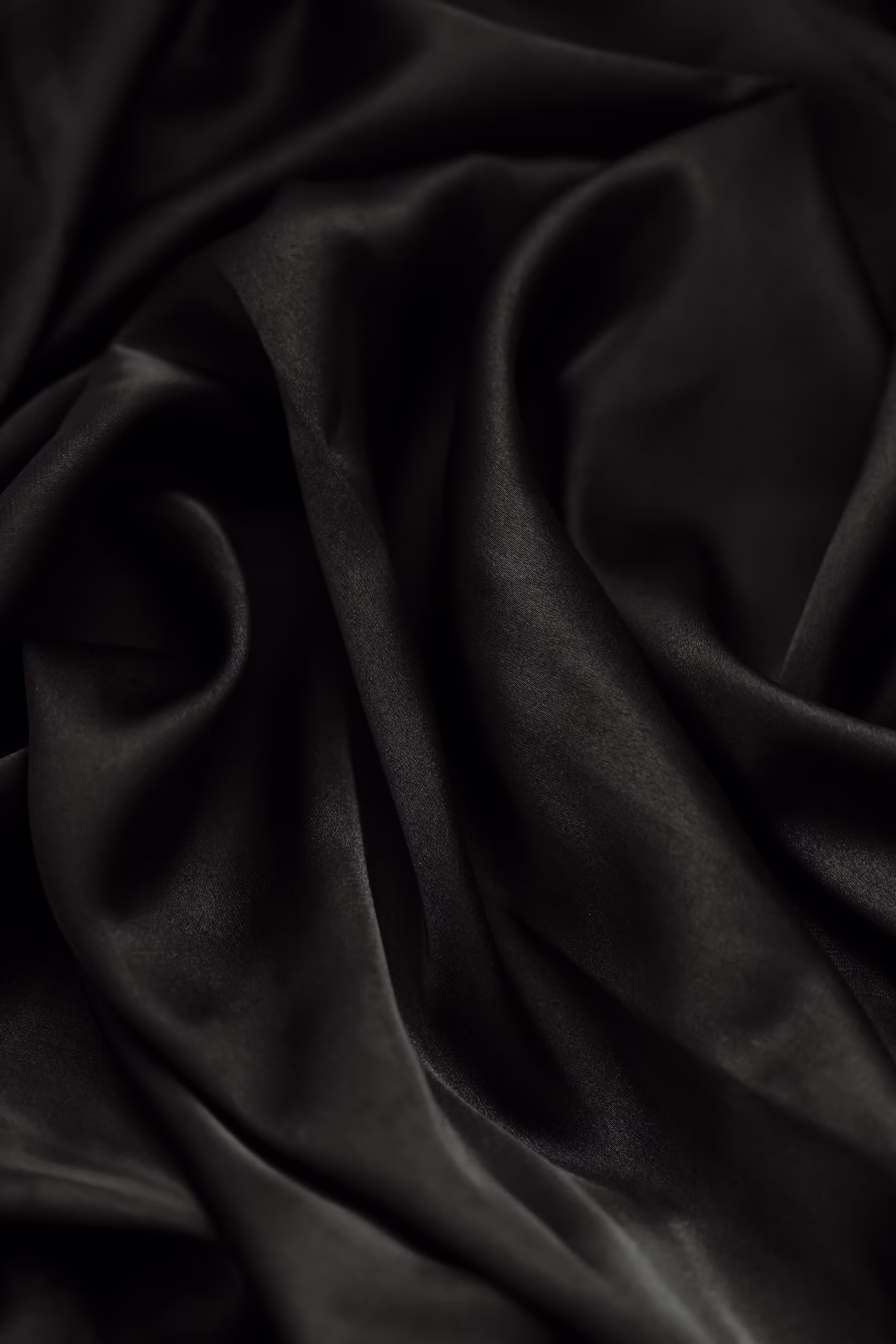 Close-up of black silky fabric with smooth folds and soft texture.